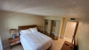 Een hotelkamer met een bed, nachtkastje, lamp, kledingkast en een spiegel.
