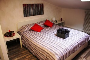 Quarto com uma cama grande, roupa de cama listrada, duas almofadas vermelhas, uma mesa de cabeceira com abajur e uma pequena prateleira com uma vela vermelha.
