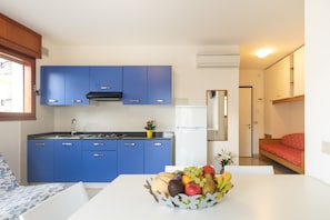 A compact kitchen with blue cabinets, a white countertop, and a fruit bowl.