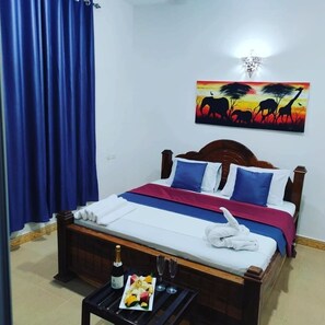 A neatly made bed with a blue and white bedspread, a wooden headboard, and a painting of a savannah scene on the wall. - Tropicana Kendwa Beach Hotel (Kendwa)