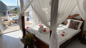 A spacious bedroom with a four-poster bed, a ceiling fan, and a large window overlooking a scenic view. - Tropicana Kendwa Beach Hotel (Kendwa)