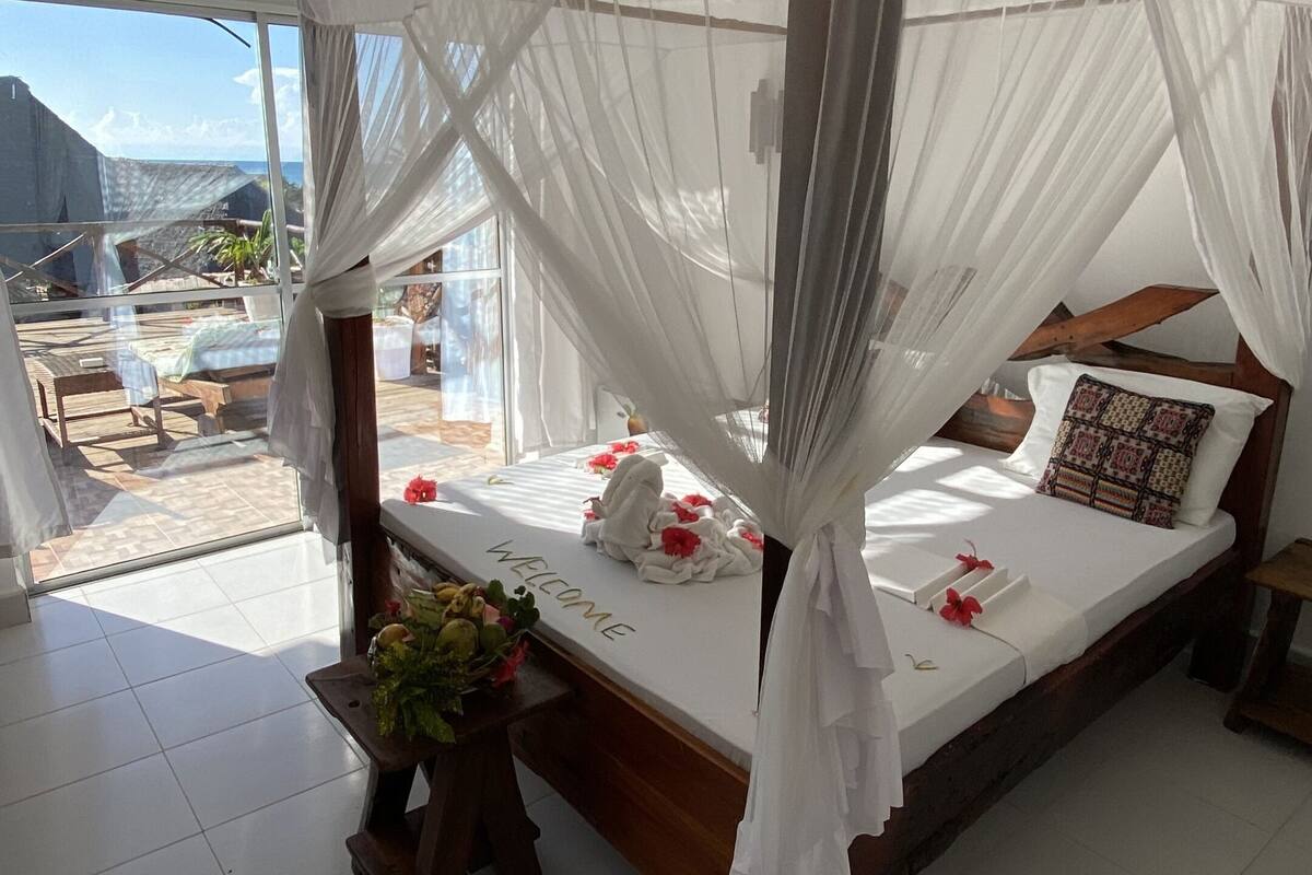 Ein geräumiges Schlafzimmer mit Himmelbett, Deckenventilator und großem Fenster mit Blick auf eine schöne Aussicht.