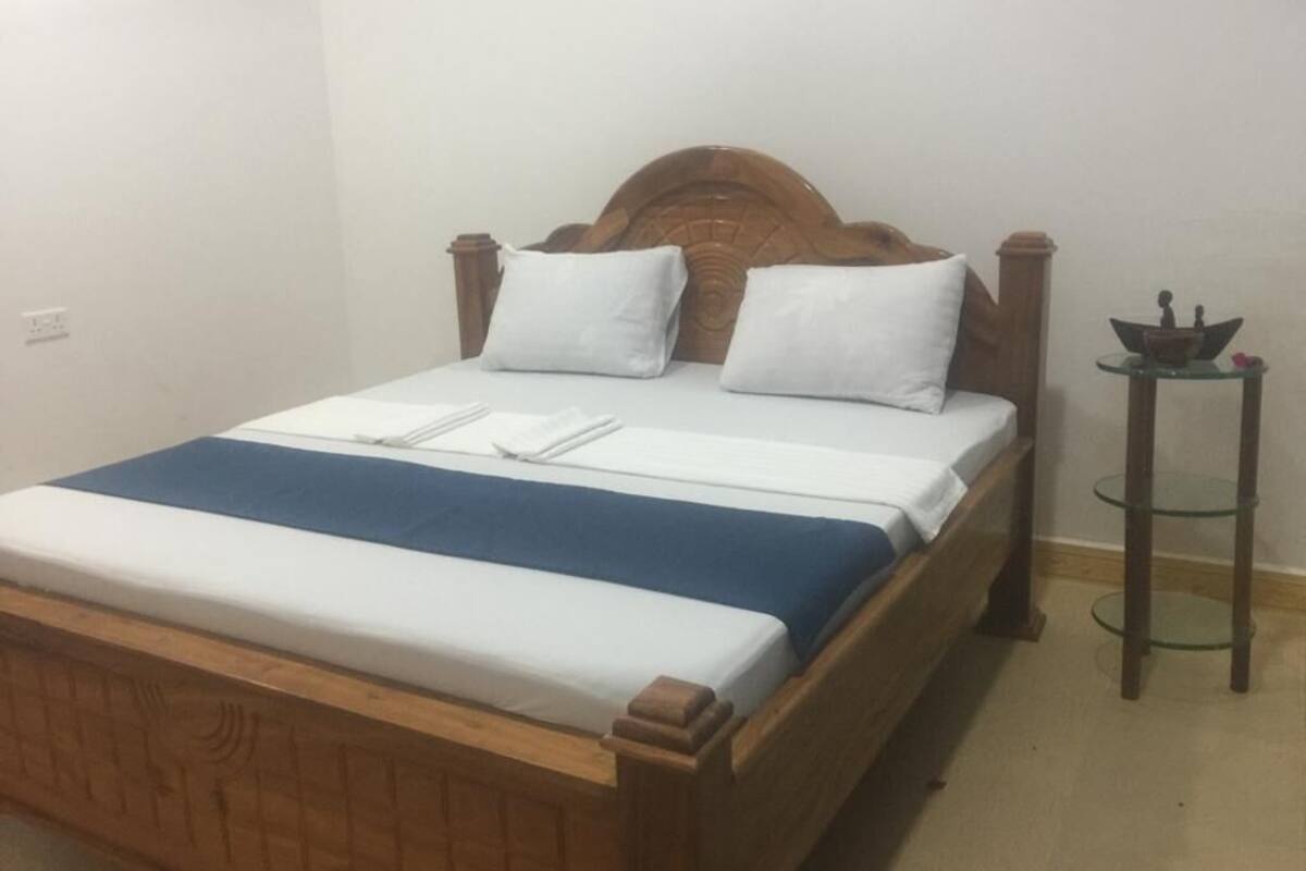 Ein ordentlich bezogenes Bett mit Holz Kopfteil, weißen Kissen und einer blauen Bettdecke.