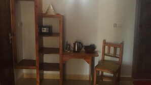 A room with a wooden table, a chair, a shelf with a radio and a kettle, and a door. - Tropicana Kendwa Beach Hotel (Kendwa)