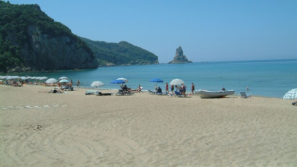 Una playa con sombrillas y sillas reclinables, un bote y un acantilado rocoso al fondo.
