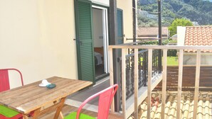 Un balcón con una mesa y sillas de madera, una puerta verde y vistas a la montaña.