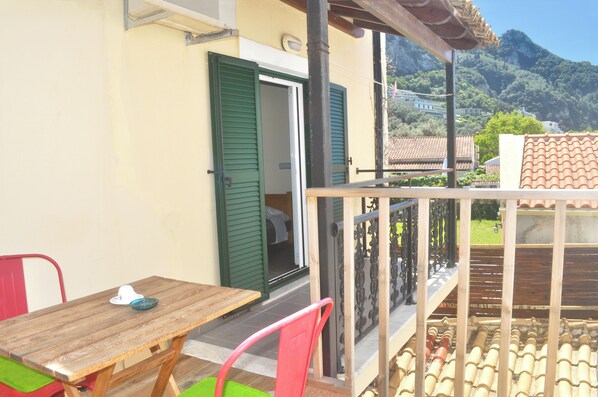 A balcony with a wooden table and chairs, a green door, and a view of a mountain.