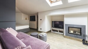 A modern living room with a sofa, ottoman, TV, fireplace, and skylights.