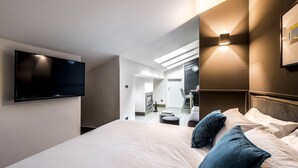 A modern hotel room with a large bed, a flat-screen TV mounted on the wall, and a small seating area with a table and chairs.