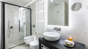 A modern bathroom with a glass-enclosed shower, a white toilet, a large vessel sink, and a mirror with a round frame.