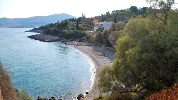 A coastal landscape with a beach, rocky shoreline, and a building with a red roof.