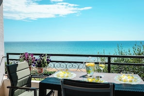 Un balcón con una mesa lista para dos personas, con vista a una playa y el mar al fondo.