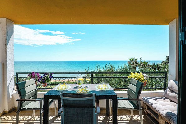 Un balcón con mesa lista para dos personas, con vista a un mar azul y despejado.