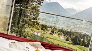 A bed with a newspaper and croissants, a window with a view of a vineyard and mountains. - Chalet Penthouse – Schenna Chalet (Schenna)