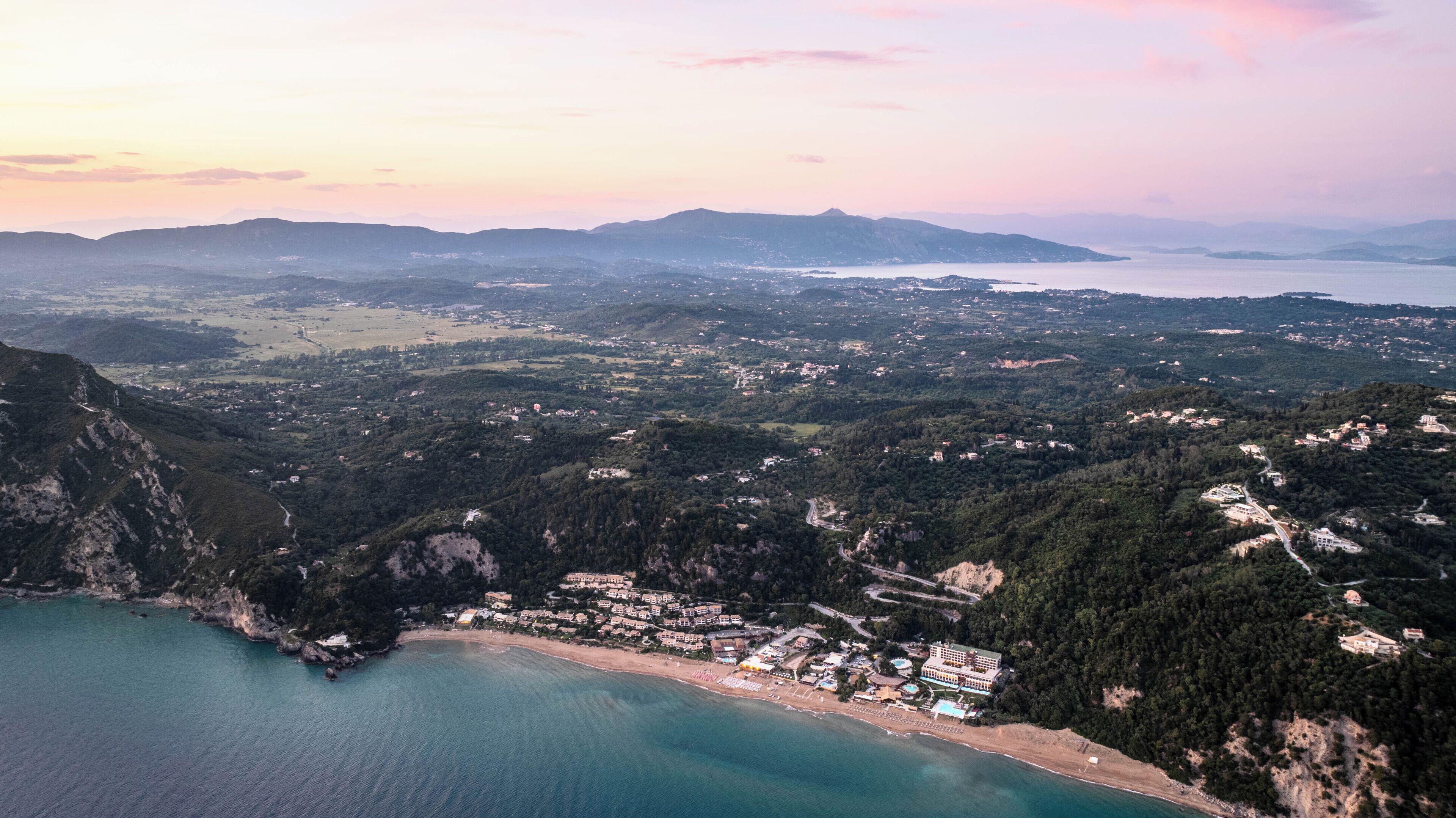 Eine Luftaufnahme einer Küstenregion mit Strand, Gebäuden und sanften Hügeln.