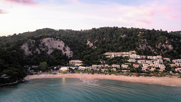 A coastal town with buildings on a hillside, a beach, and clear blue waters. - Corfu Glyfada Menigos Resort 5-8-a (Corfu)