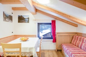 A room with a wooden ceiling, a window with a view of a snowy landscape, a table with a bowl of fruit, and a striped sofa.