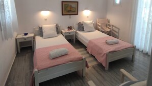 A twin bedroom with two beds, bedside tables, a nightstand, a painting, and a window. - Kikis Refurbished Apartment a Veranda Dream (Paros)