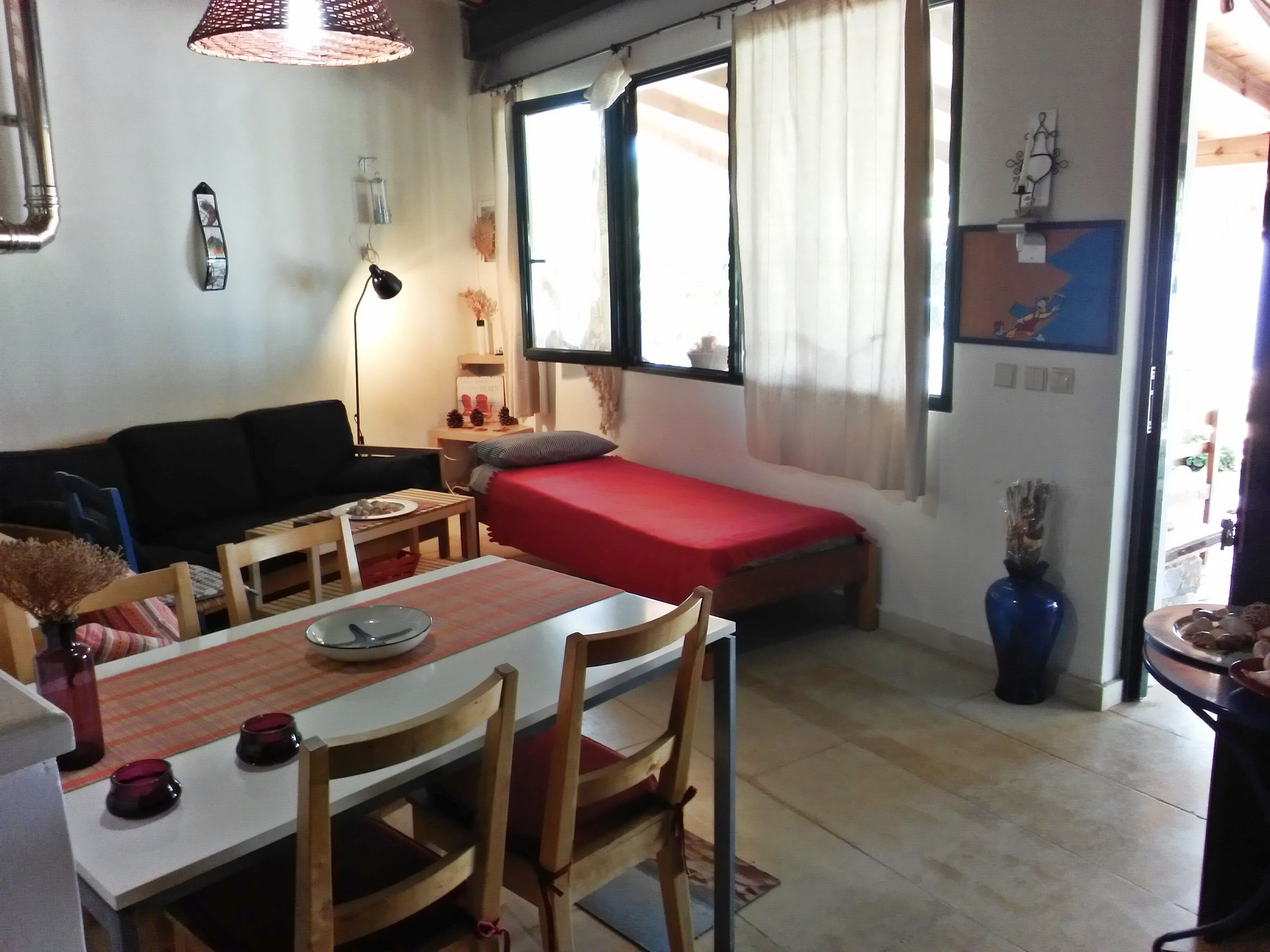 A compact living space with a bed, a small dining table, a sofa, and a window with curtains.