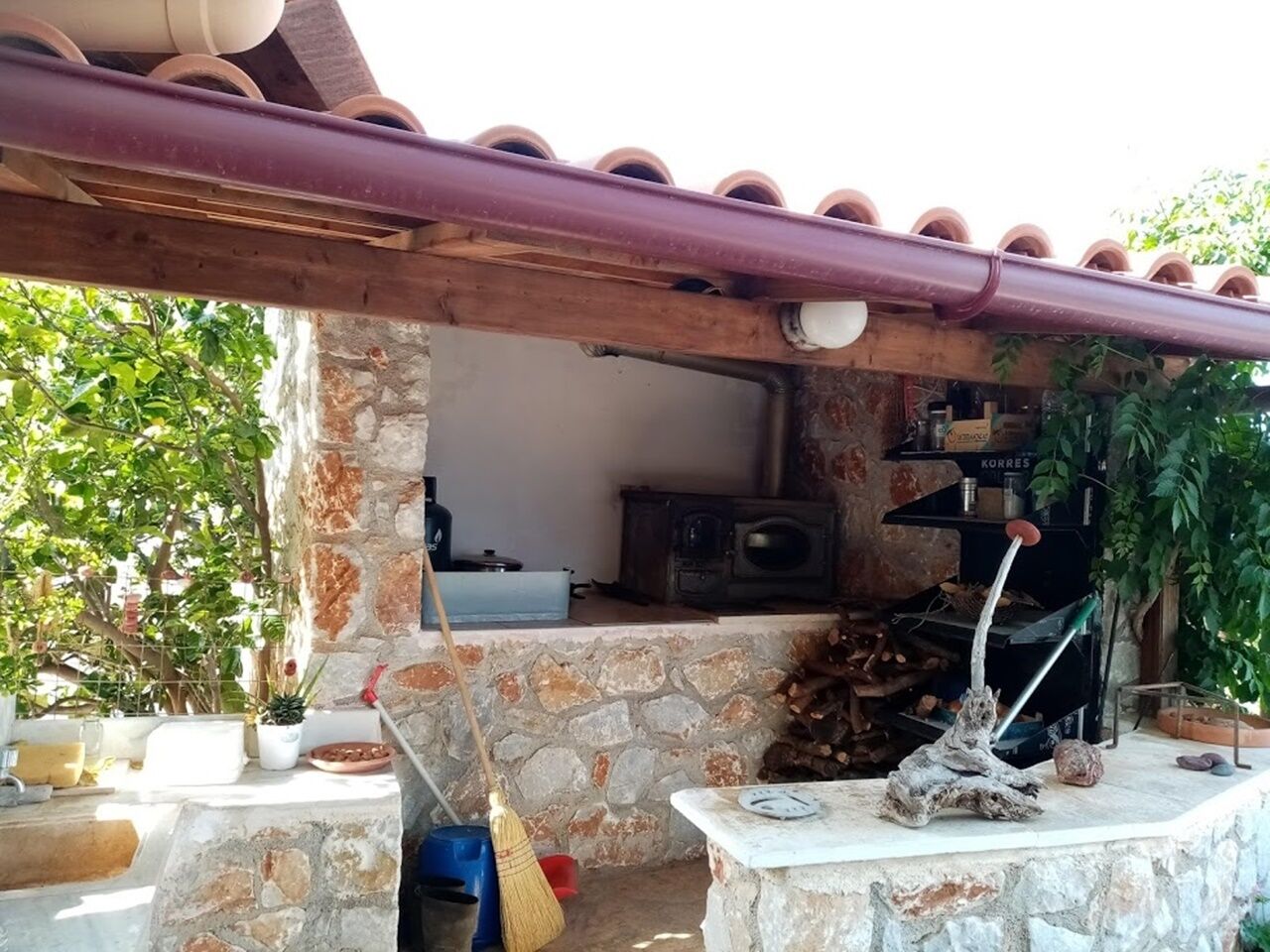Eine steinerne Außenküche im rustikalen Stil, mit Kamin, Holzregal und rustikaler Dekoration.