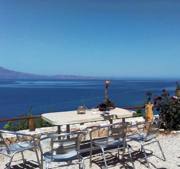 A table with chairs, a candle, and a glass of water on a terrace with a view of the sea. - Apartment Over the sea Private Place to Swim (Platanias)