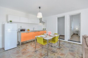 A modern kitchen with white cabinets, a white refrigerator, a microwave, and a dining table with yellow chairs.
