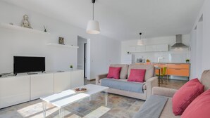 A modern living room with a sofa, coffee table, and TV. A kitchen with cabinets and a microwave is visible in the background. - Modern Apartment Casa Amanecer 1 with Pool, Terrace & Wi-Fi; Parking Available (Macher)