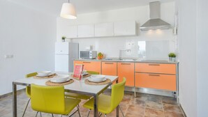 A modern kitchen with white cabinets, a microwave, and a sink. There is a dining table with chairs and a hanging light fixture. - Modern Apartment Casa Amanecer 1 with Pool, Terrace & Wi-Fi; Parking Available (Macher)
