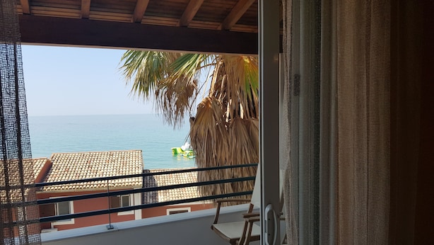 A balcony with a view of the sea, a palm tree, and a beach chair. - Glyfada Apartment Ag3g 129 (Corfu)