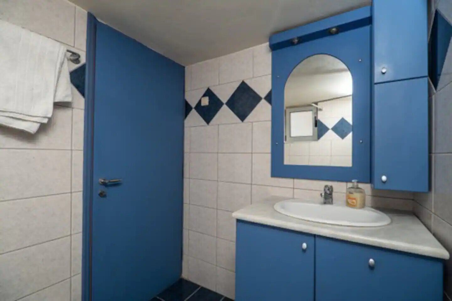 A bathroom with a blue door, a white sink, and a mirror above it.