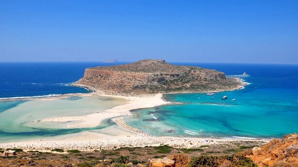 Un paysage côtier caractérisé par une île rocheuse imposante, des eaux turquoise cristallines et une plage de sable.
