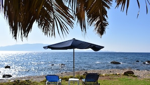 Une scène de plage avec deux chaises bleues sous un grand parasol, une petite table et un palmier au-dessus.