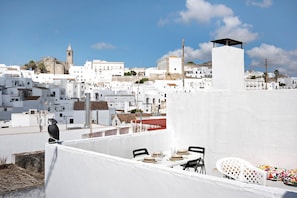 Une terrasse sur le toit avec une table dressée pour le dîner, un mur blanc et un oiseau perché sur le bord.
