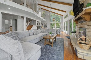 A spacious living room with a large gray sectional sofa, a wooden coffee table, and a stone fireplace. - Modern Home w/private hot tub, game room, & Amazing VIEWS (Galena)