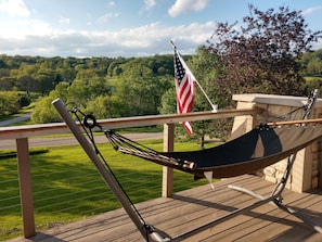 A hammock on a wooden deck with an American flag and a view of a green landscape.