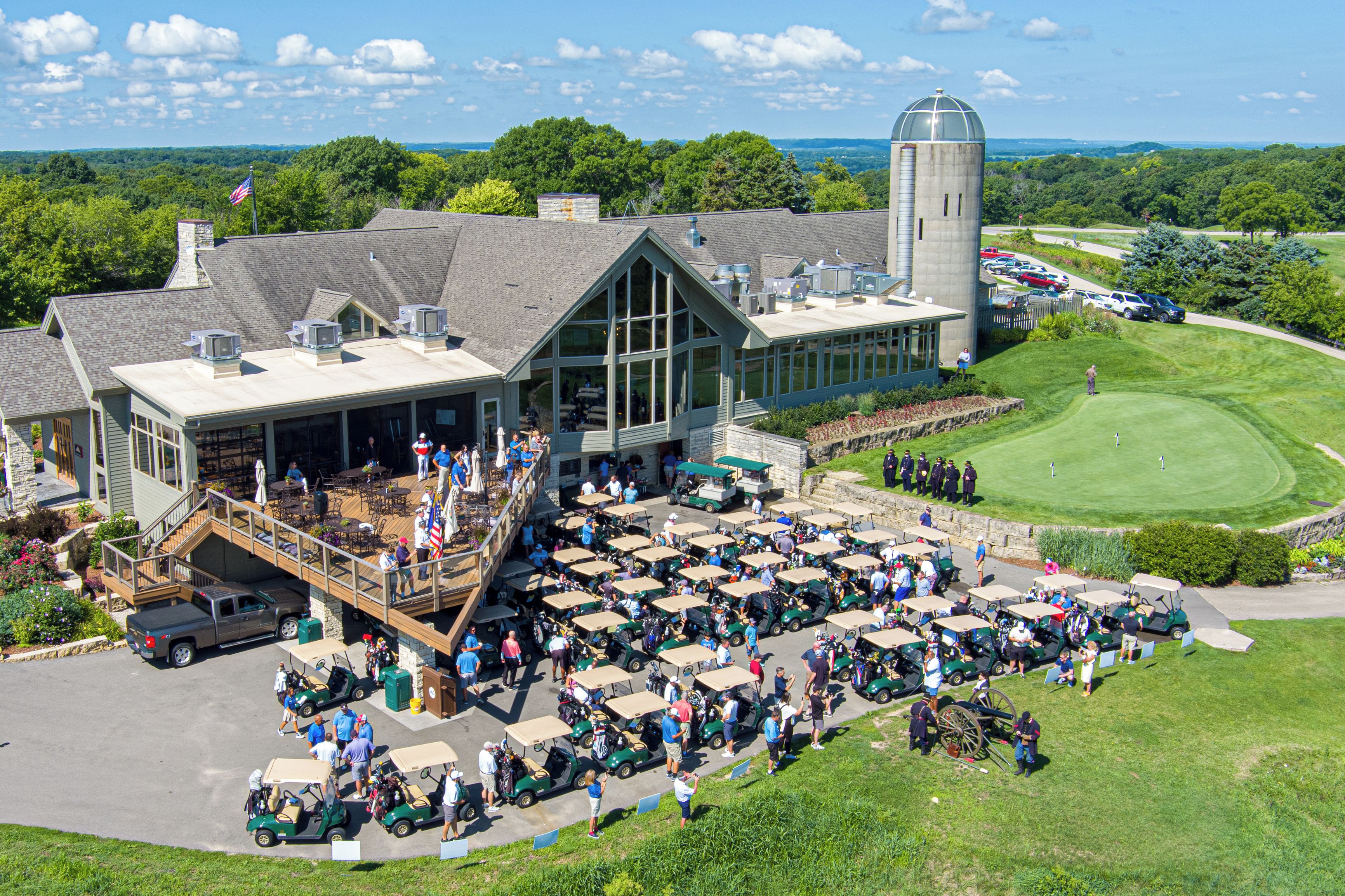 Un campo de golf con un edificio grande que tiene una terraza y zona de estar al aire libre.