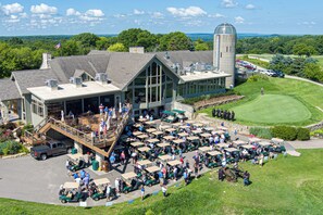 A golf course with a large building featuring a deck and outdoor seating area. - Modern Home w/private hot tub, game room, & Amazing VIEWS (Galena)