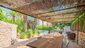 Una mesa de madera con sillas, una piscina y exuberante follaje en un patio trasero.