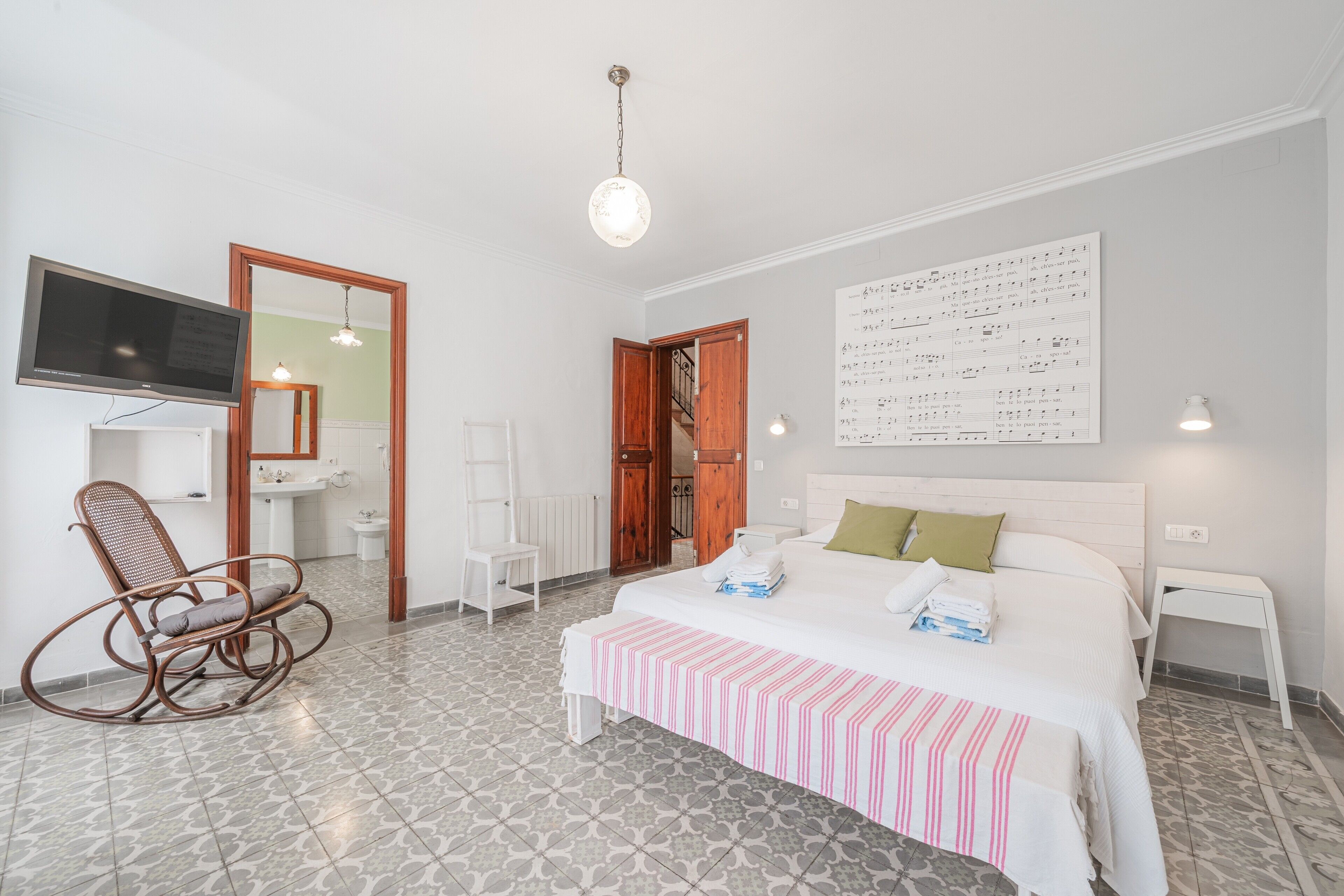 Un dormitorio con cama, televisor, espejo, silla y una pared decorada con notas musicales.