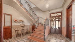 Una imponente escalera con barandillas ornamentadas, piso estampado y una puerta de madera con un panel de vidrio decorativo.