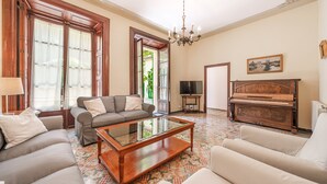 Una sala de estar con sofá, una mesa de centro de vidrio, un piano y un televisor.