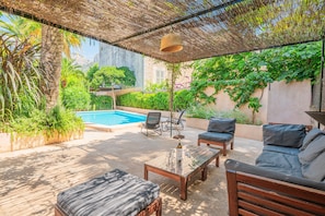 A patio area with a pool, outdoor furniture, and lush greenery.