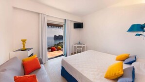 A hotel room with a bed, a sofa, a TV, and a balcony with a view of the sea.