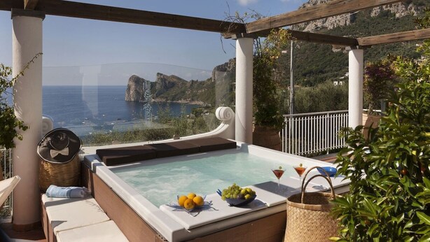 A rooftop terrace with a hot tub, outdoor seating, and a view of the sea and mountains.