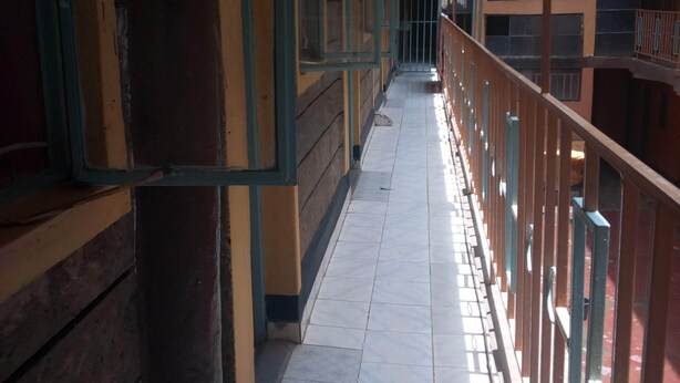 A corridor with tiled flooring, wooden benches, and metal railings. - Desmak Hotel (Isiolo)