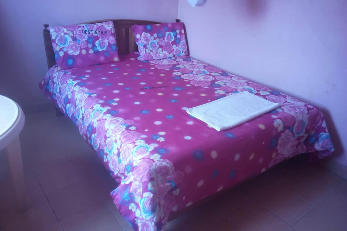 A single bed with a floral bedspread and two pillows, a white towel on the bed, and a small round table to the left.