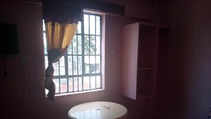 A room with a single round table, a window with bars, and a pink wall. - Desmak Hotel (Isiolo)