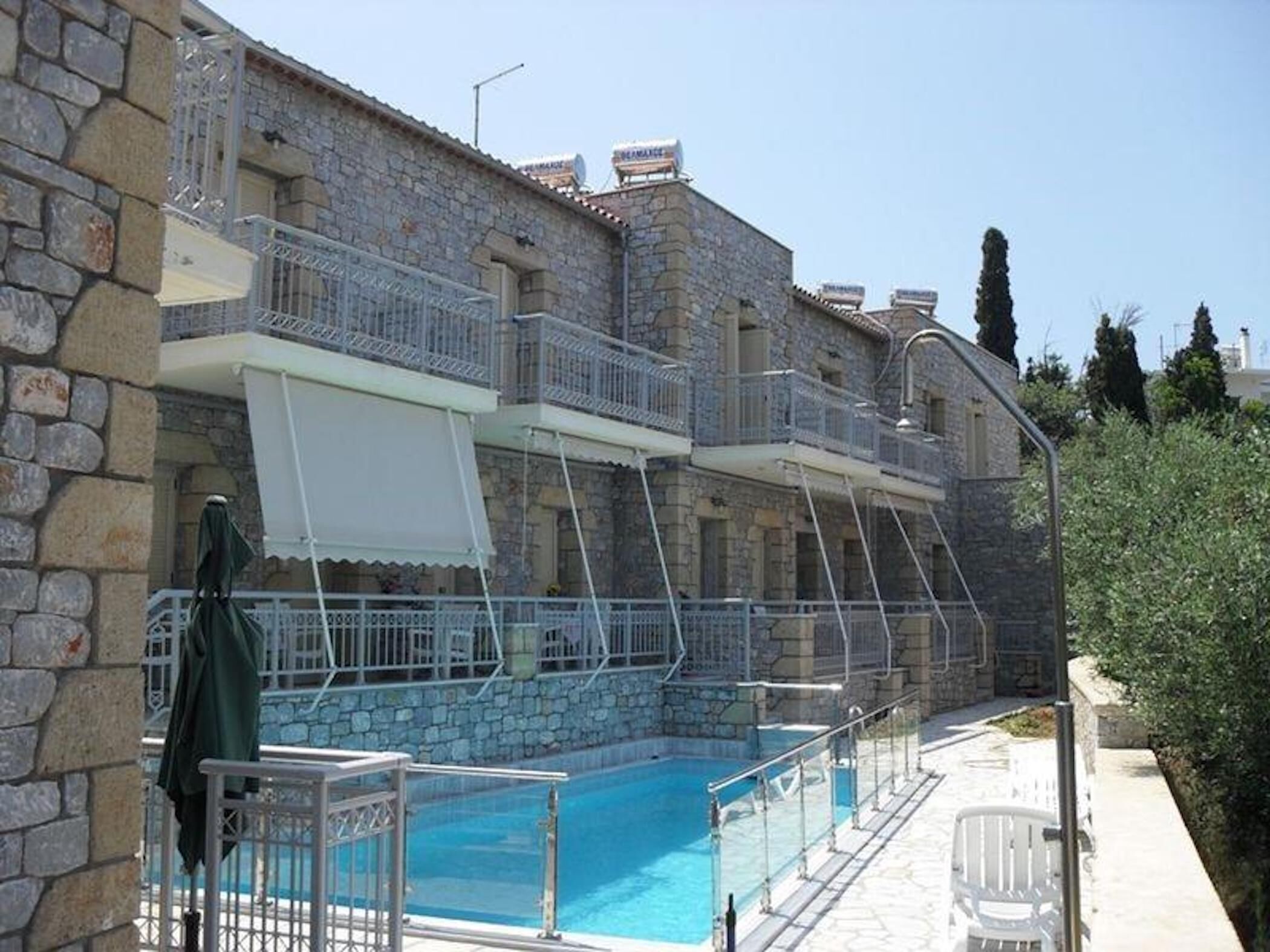A stone building with a swimming pool, balconies, and a clear sky.