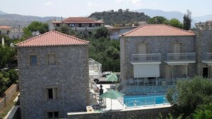 A stone building with a red-tiled roof, a pool, and a view of the surrounding landscape. - Manoleas Villas- Apartment 1 (West Mani)