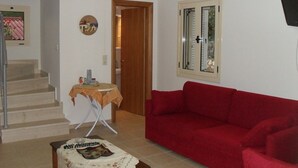 A living room with a red sofa, a small table with a decorative item, a staircase, and a door leading to another room. - Manoleas Villas- Apartment 1 (West Mani)